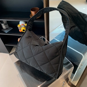 Detailed macro view of black quilted nylon pillow bag on minimalist acrylic stand display