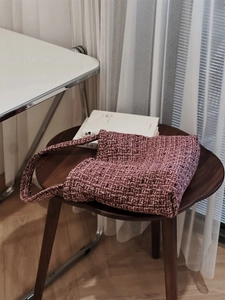 Primo piano della borsa a spalla in tweed intrecciato rosa e viola su uno sgabello