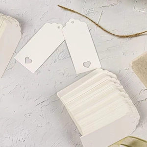 White heart-shaped cutout paper gift tags on grey texture with rustic jute rope