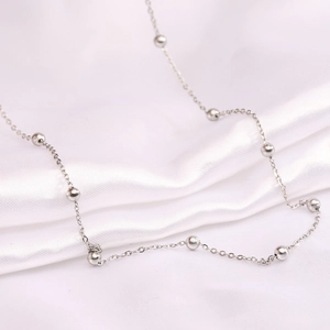 Macro shot of silver stainless steel bead chain on white silk showing elegant details