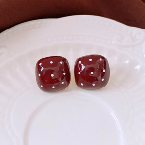 Close-up of square burgundy resin earrings with white polka dots on a white relief plate