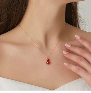 Detail of a natural red agate gourd pendant on a golden chain worn by a model