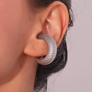 Macro view of C-shaped silver ear cuff with textured scale pattern on a female model