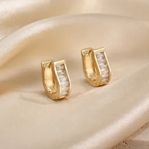 Macro shot of gold U-shaped earrings with rectangular zircons on champagne silk