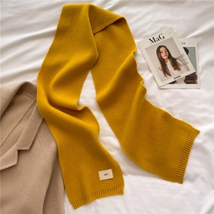 Close-up of yellow knit scarf with emo tag on soft fabric against beige coat and magazines