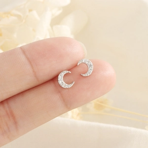 Macro detail of crescent moon stud earrings with pavé zircons held between fingers
