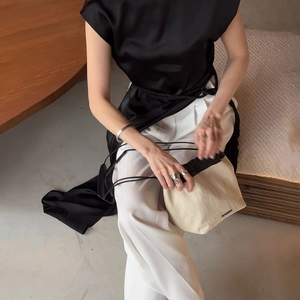 Detail view of elegant sleeveless satin top paired with white trousers and canvas tote bag