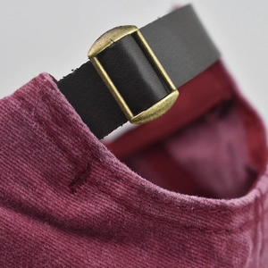 Close-up of burgundy corduroy baseball cap with leather strap and bronze metal buckle