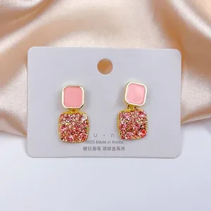 Macro shot of pink enamel square earrings with sparkling crystals on a silk backdrop