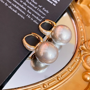 Close-up of gold zircon ear clips with large grey pearls on a vintage mirror surface