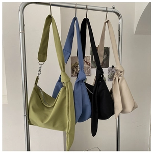 Four minimalist canvas crossbody bags in green, blue, black, and white colors with knot straps
