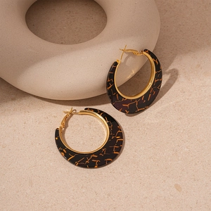 Close-up of tortoise shell resin hoop earrings with gold texture on beige background