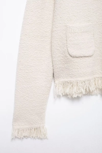Detailed close-up of cream knit cardigan featuring fringe trim and textured tweed fabric