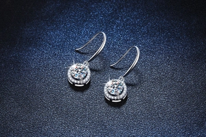 Close-up of S925 silver halo earrings with round moissanite drop hooks on a dark blue background