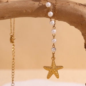 Close-up of a 18K gold-plated starfish and pearl necklace on a natural wood branch