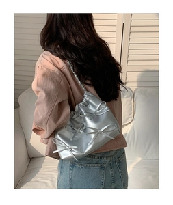 Silver shoulder bag with 3D bows and chain strap worn over the shoulder by a model