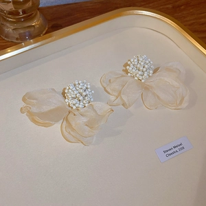 Close-up of beige fabric flower earrings with white beaded centers on a gold tray