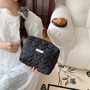 Lifestyle shot of black quilted heart makeup bag with white label held by a model