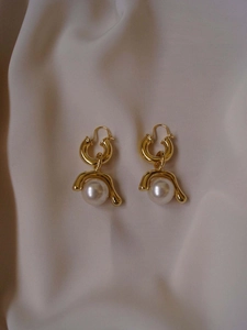 Detailed macro shot of vintage gold pearl earrings on elegant cream satin fabric