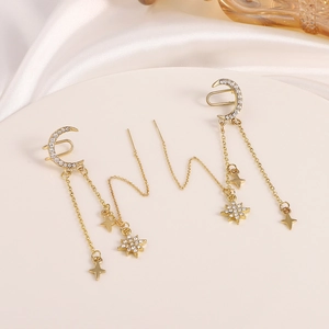 Golden moon and star tassel earrings with zircon studs on white silk fabric background