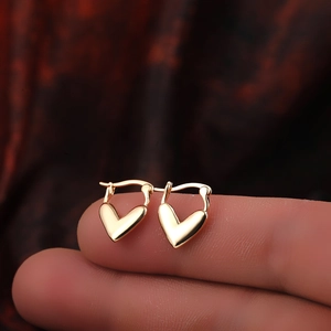Close-up of 18K gold heart-shaped earrings with zircon inlay held on fingers