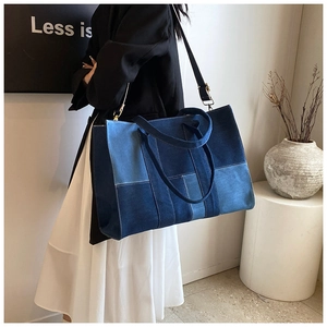 Detail of large denim patchwork tote bag with white stitching and long shoulder strap