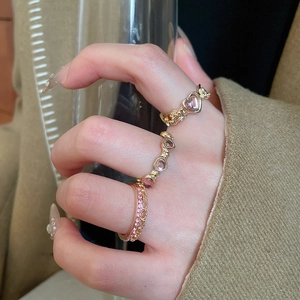 Detailed close-up of golden ring set featuring pink zircon hearts and wings design