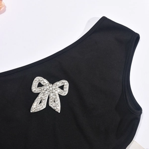 Detail of silver rhinestone bow accent on a black one-shoulder dress with soft fabric texture