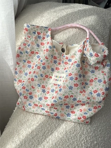 Detailed macro view of floral cotton tote bag with brand label on soft white chair