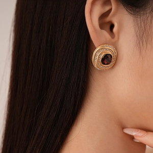 Detailed close-up of vintage oval gold earrings with red gemstone and white crystals