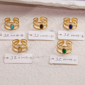 Five gold open rings with natural stones and hollow layers on white textured background