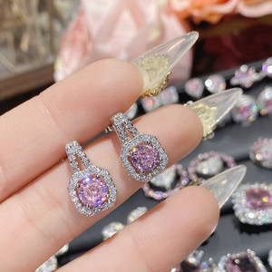 Pink gemstone halo earrings in silver setting held against a warm floral background