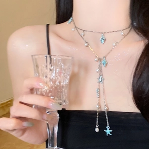 Detailed close-up of a silver Y-necklace with blue starfish and pearl charms on a model