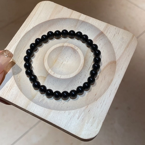 Close-up of 8-10mm black obsidian beaded bracelet on a light wood jewelry display tray