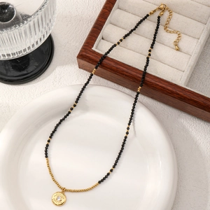 Minimalist evil eye beaded necklace with black faceted stones and gold pendant on a ceramic plate