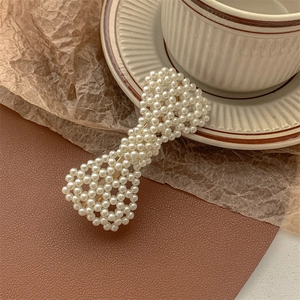 Close-up of a handmade pearl bow hair clip with gold metal base on vintage background
