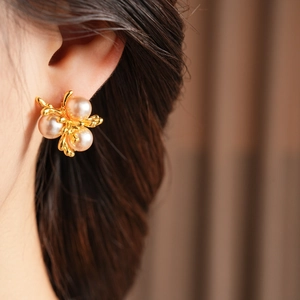 Close-up of gold branch earrings with pink pearls worn by a model in soft lighting