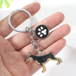 Macro detail of metal keychain featuring Doberman and paw print charms held by hand