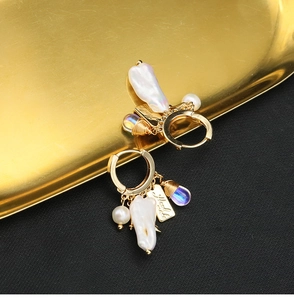 Close-up of golden round earrings with baroque pearl and blue glass waterdrop charms