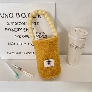 Detail of yellow fuzzy lamb wool cup carrier bag with cute black cat patch and plaid handle