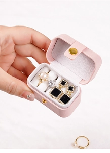 Close-up of a pink mini travel jewelry box with rings and earrings held by a model