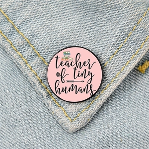 Round pink teacher of tiny humans brooch badge pinned on blue denim fabric