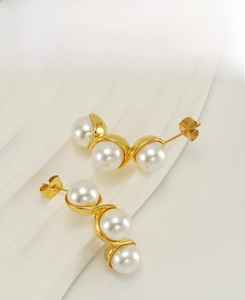 Detail of three white pearls set in a curved gold stainless steel stud earring