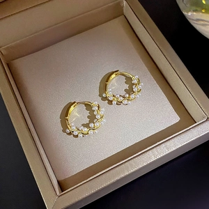 Close-up of golden hoop earrings with small pearls on a champagne velvet jewelry box