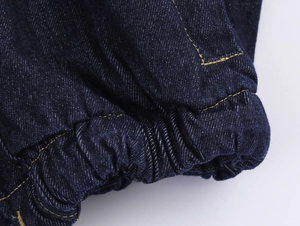 Détail du poignet de veste en jean bleu foncé avec coutures jaunes et texture élastique