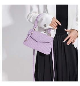Detail of purple woven crossbody bag featuring a knotted handle and metallic hardware strap