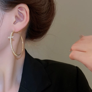 Gros plan d'une boucle d'oreille créole dorée avec pendentif croix en strass brillants