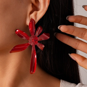 Close-up of a model wearing large layered red floral earrings with a glossy finish