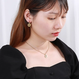 Gros plan sur l'ensemble collier et boucles d'oreilles boussole en acier doré 18k