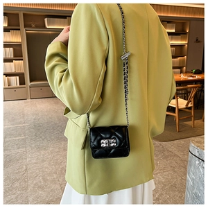 Close-up of a black quilted crossbody bag with metal chain strap and square buckle